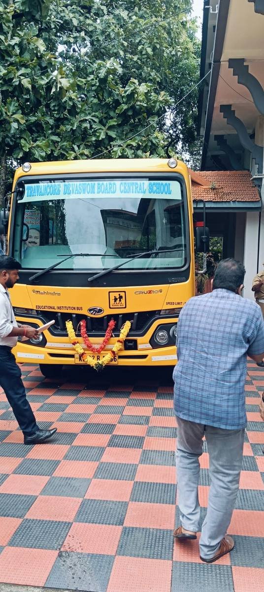 The school bus head-on under the portico, its windscreen lettered Travancore Devaswom Board Central School.