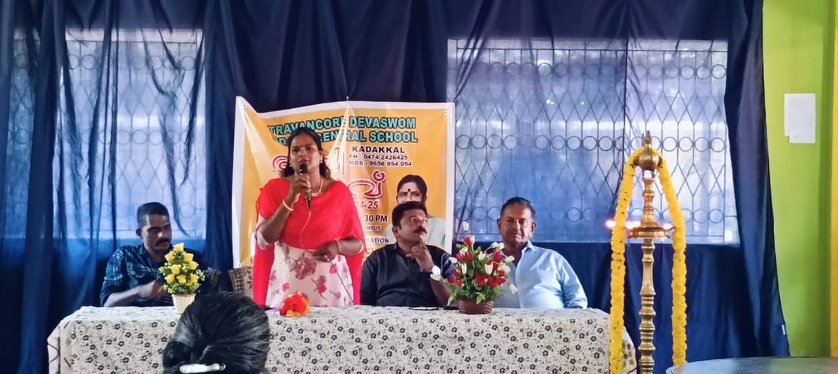 A speaker addressing the gathering at the food fest, the school's banner on the wall behind.