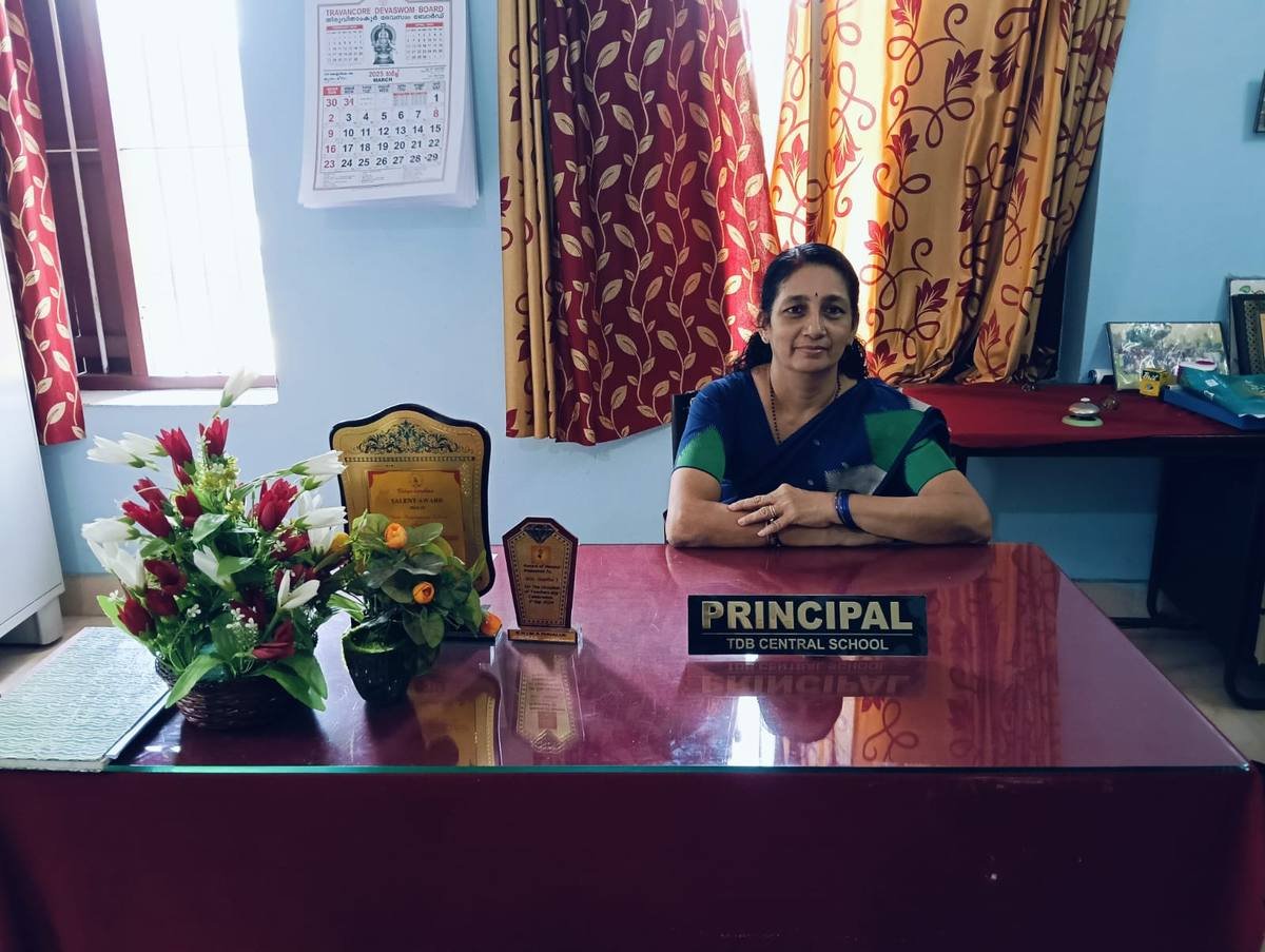 The Principal seated at her desk, the nameplate reading Principal, TDB Central School in front of her.