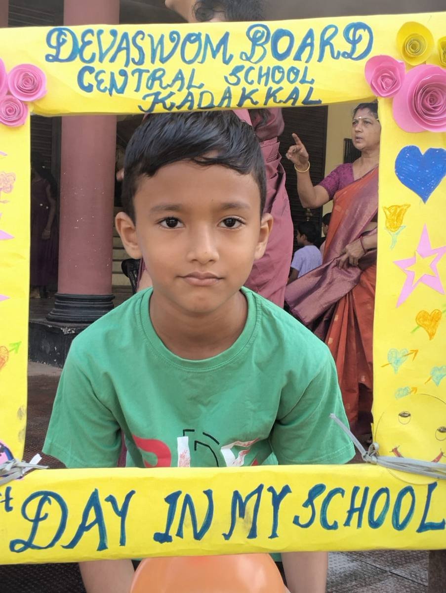 A young boy in a green T-shirt looking out through the decorated photo frame.