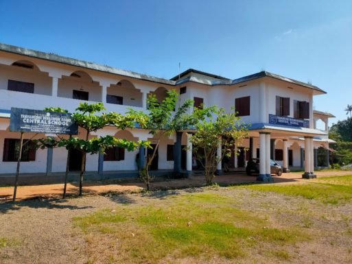 The school seen from the gate, its name board under the trees.