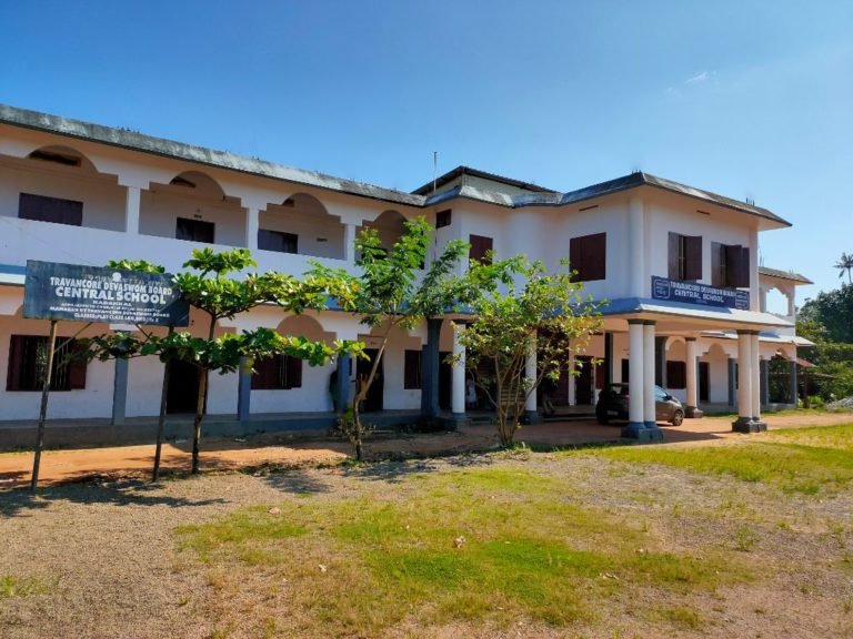 The school seen from the gate, its name board under the trees.