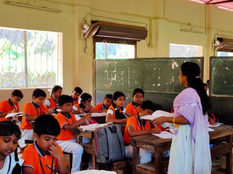 A teacher moving through the class while pupils work at their desks.